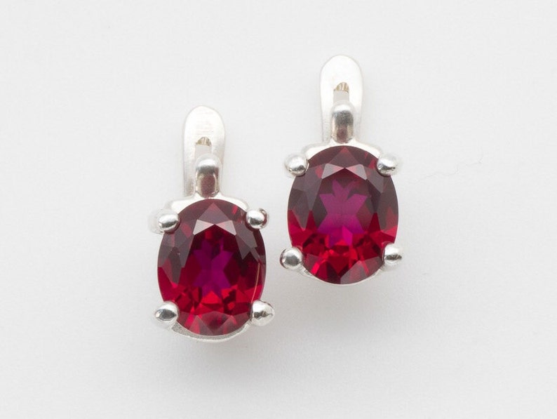 May include: A pair of silver earrings with red oval-shaped gemstones.