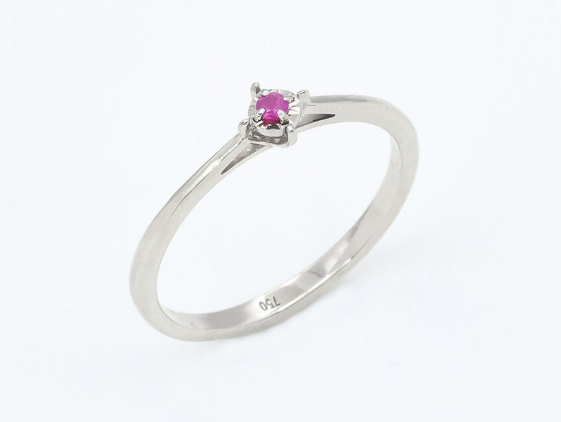 Puede incluir: Un delicado anillo de plata con una peque&ntilde;a piedra preciosa rosa brillante engastada en una sencilla garra. El anillo est&aacute; marcado con "750" en la banda interior.