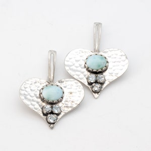 May include: A pair of silver heart-shaped earrings with a light blue gemstone and clear rhinestones.