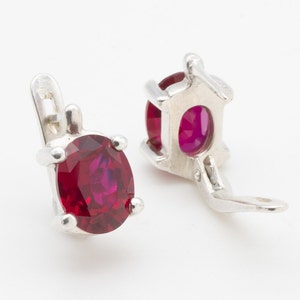 May include: A pair of silver earrings with red oval-shaped gemstones. The earrings have a clip-on closure.