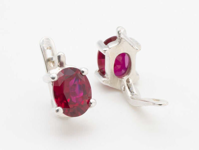 May include: A pair of silver earrings with red oval-shaped gemstones. The earrings have a clip-on closure.