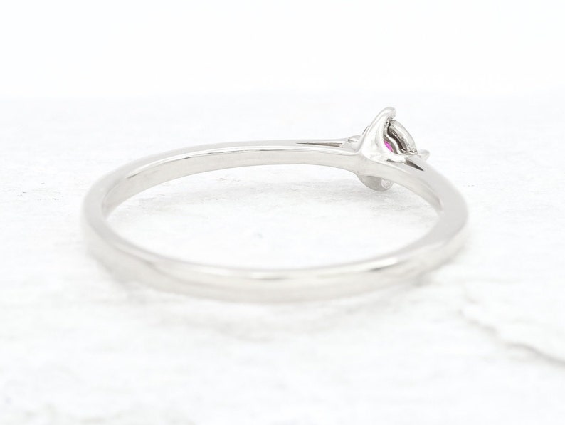 Puede incluir: Un anillo de banda de plata simple con una sola piedra preciosa rosa engastada en una configuraci&oacute;n de garras.
