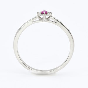 Puede incluir: Un anillo de banda de plata simple con una sola piedra preciosa de rub&iacute; engastada en un engaste de cuatro garras.