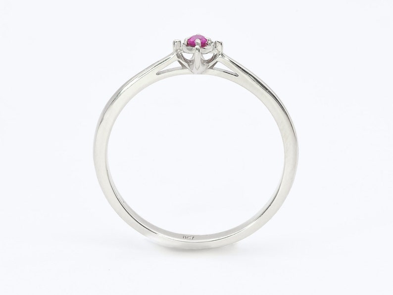 Puede incluir: Un anillo de banda de plata simple con una sola piedra preciosa de rub&iacute; engastada en un engaste de cuatro garras.