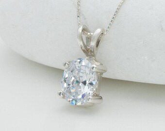May include: A silver pendant necklace featuring a large, oval-cut, clear gemstone. The gemstone is held in place by four prongs on a silver setting. The necklace chain is a delicate silver box chain. The pendant is displayed against a white background.