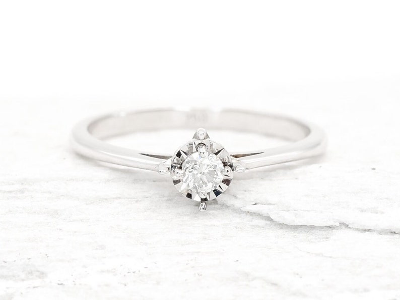 May include: A simple solitaire engagement ring with a single round diamond set in a white gold band.