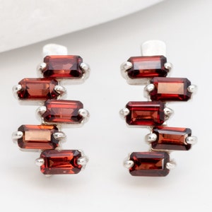May include: A pair of silver earrings with a cascade of six red garnet stones in a rectangular shape.