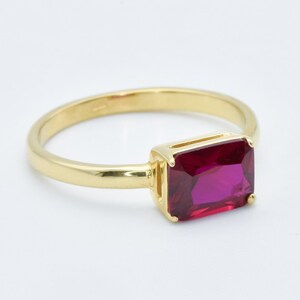 Puede incluir: Un anillo de oro con una piedra preciosa rectangular grande de color rojo oscuro.