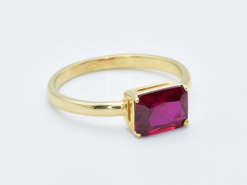 Puede incluir: Un anillo de oro con una piedra preciosa rectangular grande de color rojo oscuro.