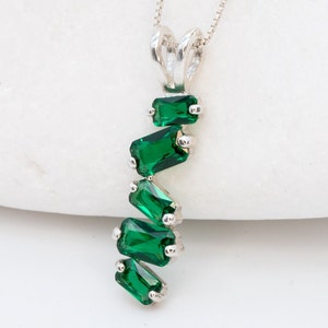 May include: A silver necklace with a pendant featuring a cascade of emerald green crystals.