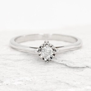 May include: A simple silver band ring with a single round diamond set in a four-prong setting.