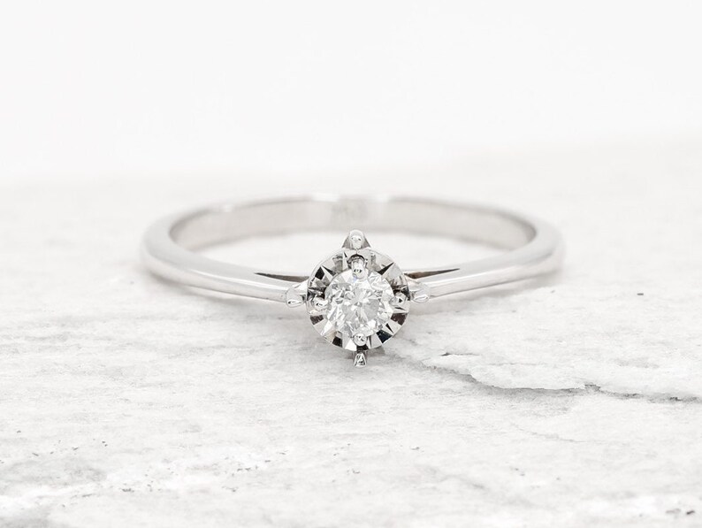 May include: A simple silver band ring with a single round diamond set in a four-prong setting.