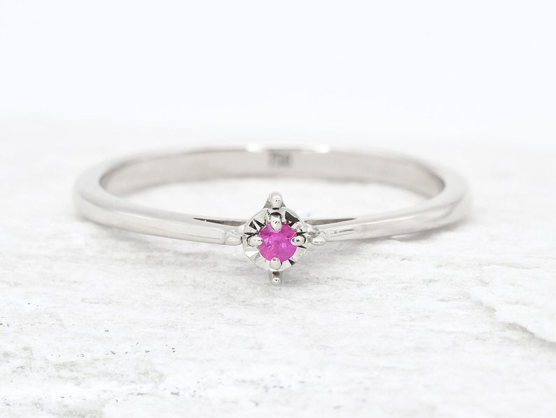 Puede incluir: Un delicado anillo de plata con una peque&ntilde;a piedra preciosa rosa engastada en un engaste de cuatro garras.