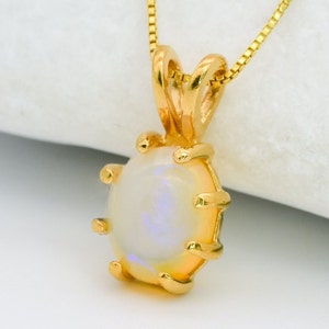 May include: A gold pendant necklace featuring a white opal gemstone set in a gold bezel setting. The pendant hangs from a delicate gold chain.