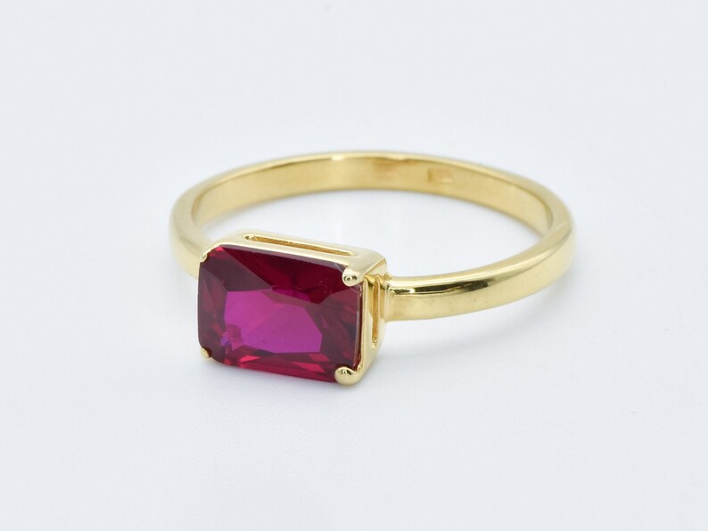 Puede incluir: Un anillo de oro con una piedra preciosa rectangular grande de color rojo oscuro.