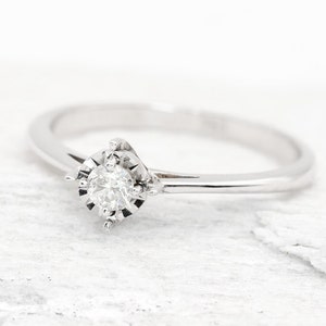 May include: A simple silver band ring with a single round diamond set in a delicate, prong-style setting.