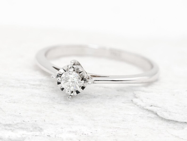 May include: A simple silver band ring with a single round diamond set in a delicate, prong-style setting.