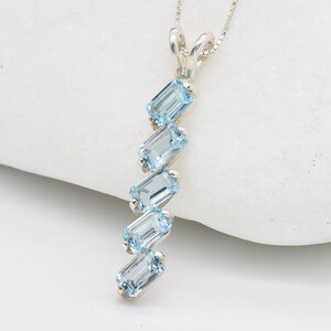 Op de afbeelding: Een zilveren ketting met een hanger met een waterval van zes lichtblauwe topaas edelstenen in smaragd-slijpsel.