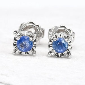 May include: A pair of silver stud earrings with a small, round, blue sapphire gemstone in each earring.