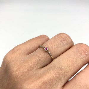 Puede incluir: Un delicado anillo de oro con una peque&ntilde;a piedra roja brillante.