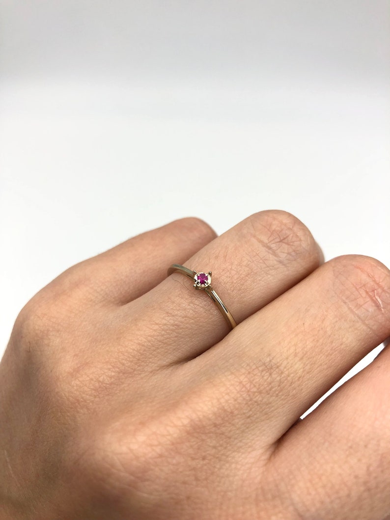 Puede incluir: Un delicado anillo de oro con una peque&ntilde;a piedra roja brillante.