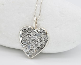 May include: A silver heart-shaped pendant necklace with a detailed design of circles and swirls.
