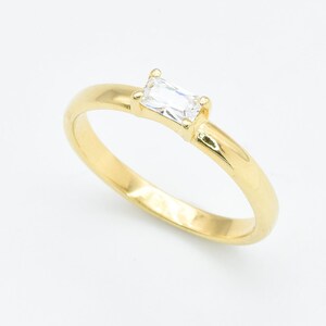 Op de afbeelding: Een gouden ring met een enkele, heldere, rechthoekige edelsteen.