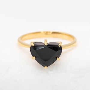 Op de afbeelding: Een gouden ring met een zwarte hartvormige edelsteen.