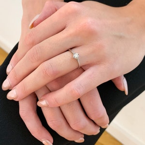May include: A simple solitaire engagement ring with a single round diamond set in a thin band.