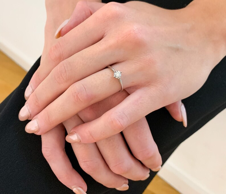 May include: A simple solitaire engagement ring with a single round diamond set in a thin band.