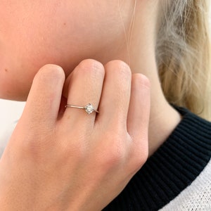 May include: A simple solitaire ring with a single round diamond set in a thin band.