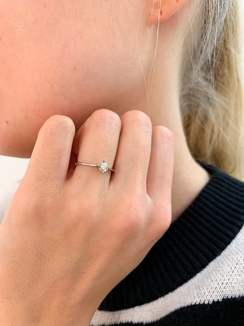 May include: A simple solitaire ring with a single round diamond set in a thin band.