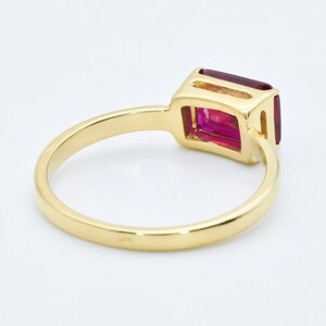 Puede incluir: Un anillo de oro con una gran piedra preciosa rectangular de color rosa. El anillo es simple y elegante.