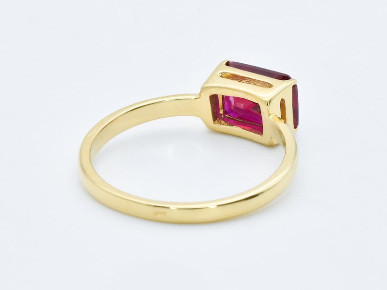 Puede incluir: Un anillo de oro con una gran piedra preciosa rectangular de color rosa. El anillo es simple y elegante.