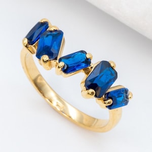 May include: A gold ring with five blue rectangular gemstones set in a staggered pattern.