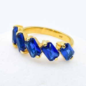 May include: A gold ring featuring a row of blue gemstones. The gemstones are set in a staggered pattern and are rectangular in shape.