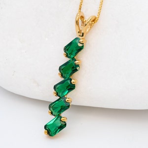 May include: A gold necklace with a pendant featuring a cascade of emerald green rectangular stones.