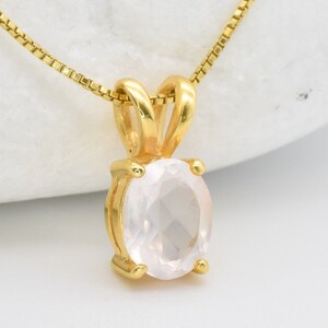May include: A gold chain necklace with a pendant featuring a clear oval-shaped rose quartz gemstone.