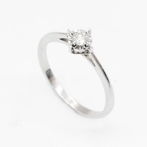 May include: A simple silver band ring with a single round diamond set in a four-prong setting.