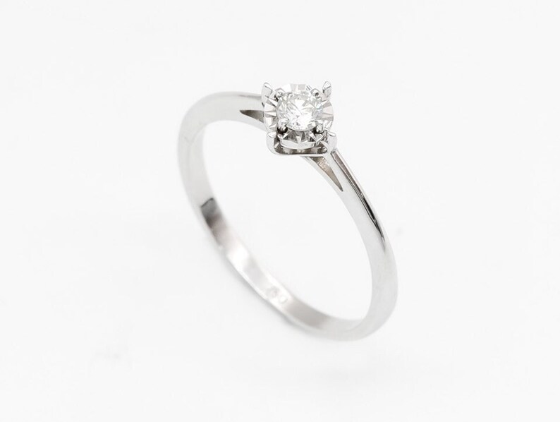 May include: A simple silver band ring with a single round diamond set in a four-prong setting.
