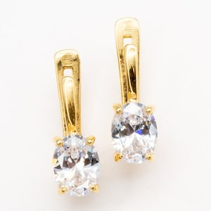 May include: A pair of gold earrings with oval-shaped clear cubic zirconia stones.