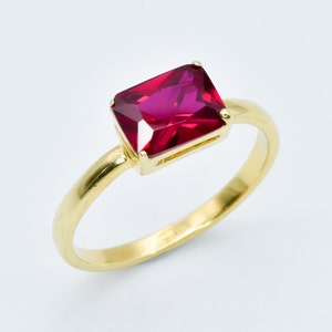 May include: A gold ring with a large, rectangular, red gemstone.
