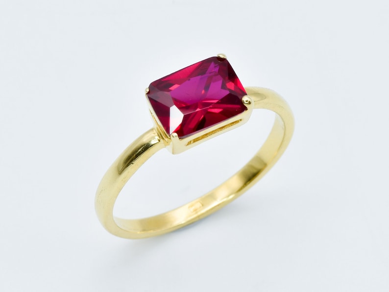 Puede incluir: Un anillo de oro con una piedra preciosa roja rectangular grande.