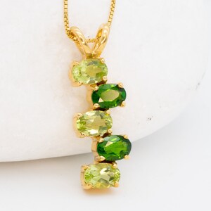 May include: A gold necklace with a pendant featuring a cascade of oval-shaped green and light green gemstones.