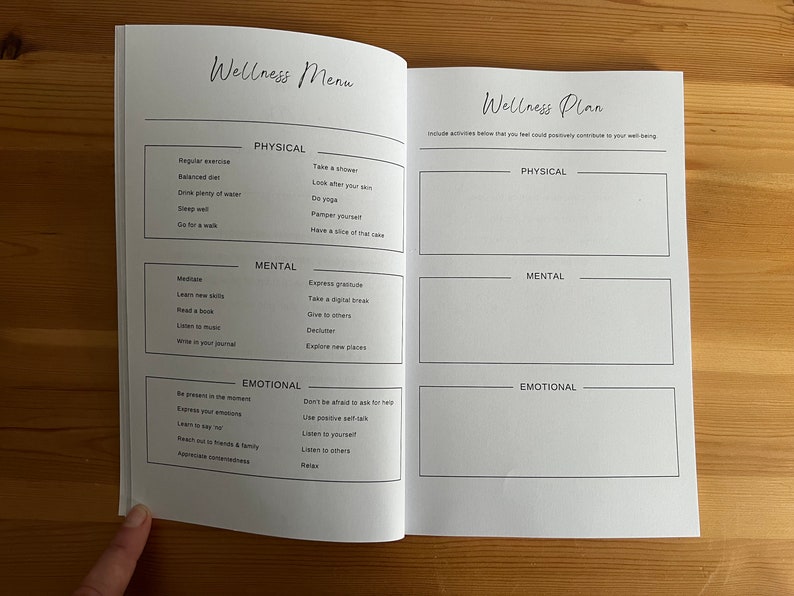 May include: A white wellness planner with a black and white design. The planner is divided into three sections: physical, mental, and emotional. Each section has a list of activities that can help improve well-being. The planner also includes a section for creating a personalized wellness plan.
