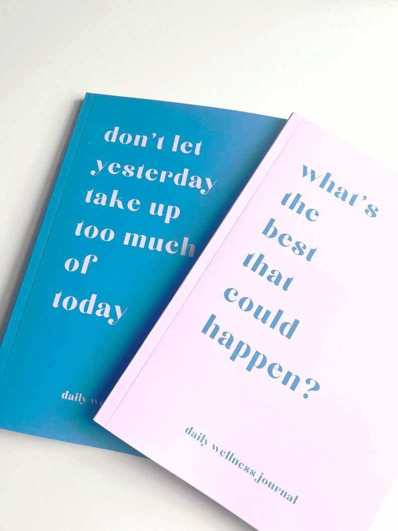 May include: Two pink and blue daily wellness journals with the text "don't let yesterday take up too much of today" on the blue journal and "what's the best that could happen?" on the pink journal.