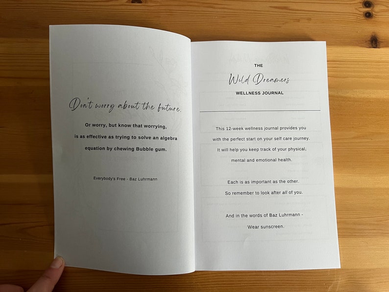 May include: An open book with a white background and black text. The left page has a quote about worrying, and the right page has the title "The Wild Dreamers Wellness Journal" and a description of the journal. The quote on the left page reads: "Don't worry about the future. Or worry, but know that worrying, is as effective as trying to solve an algebra equation by chewing Bubble gum. Everybody's Free - Baz Luhrmann"
