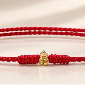 Peut inclure: Un bracelet en cordon tressé rouge avec une petite breloque dorée en forme de gourde. La breloque est gravée d'un caractère chinois. Le bracelet est composé d'un fil rouge fin et tressé avec des nœuds réglables de chaque côté de la breloque.