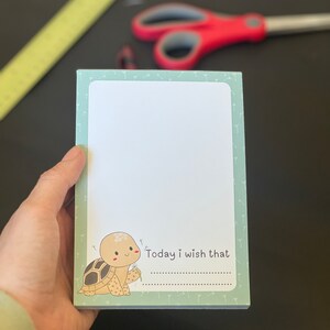 May include: A green notepad with a white border and a cute cartoon turtle holding a dandelion. The notepad has the text "Today I wish that" printed on it.