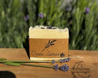 Puede incluir: Una pastilla de jabón de lavanda orgánica envuelta en papel marrón con un diseño de flor de lavanda y el texto "Organic Lavender".